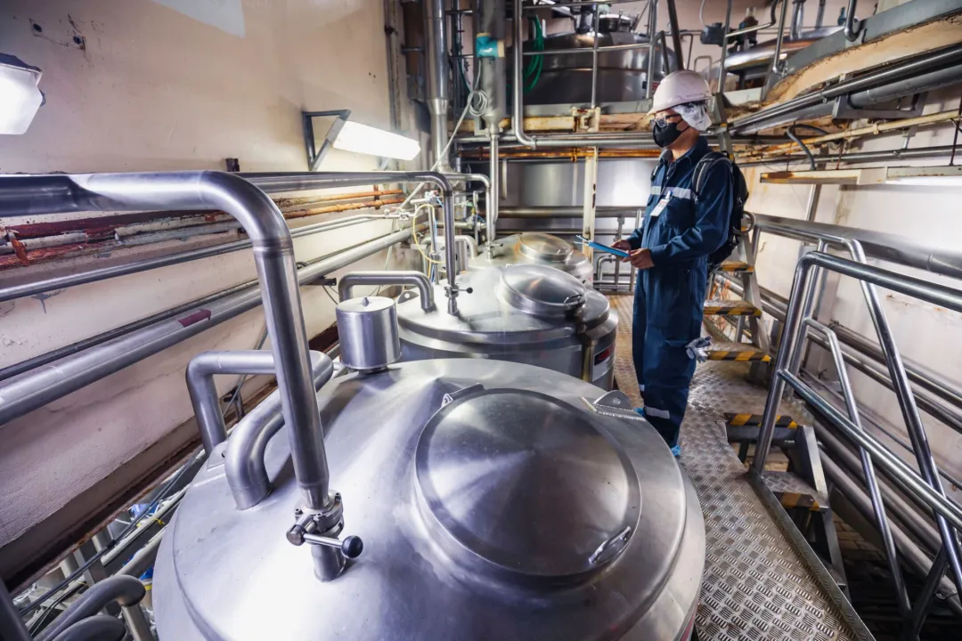 Worker beside stainless steel tanks in a food processing plant