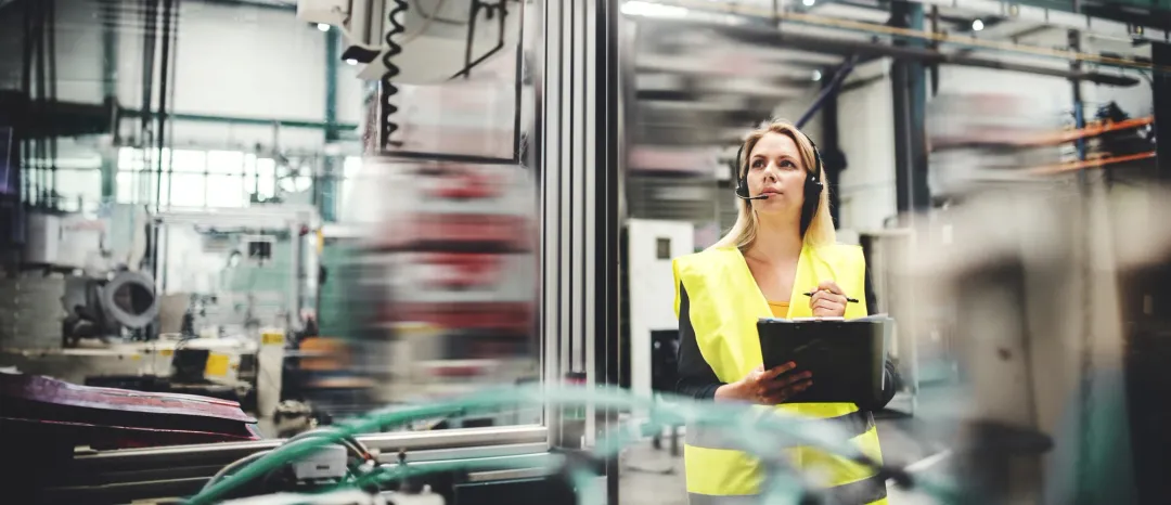 Guide in a safety vest wearing a headset and holding a clipboard in a plant