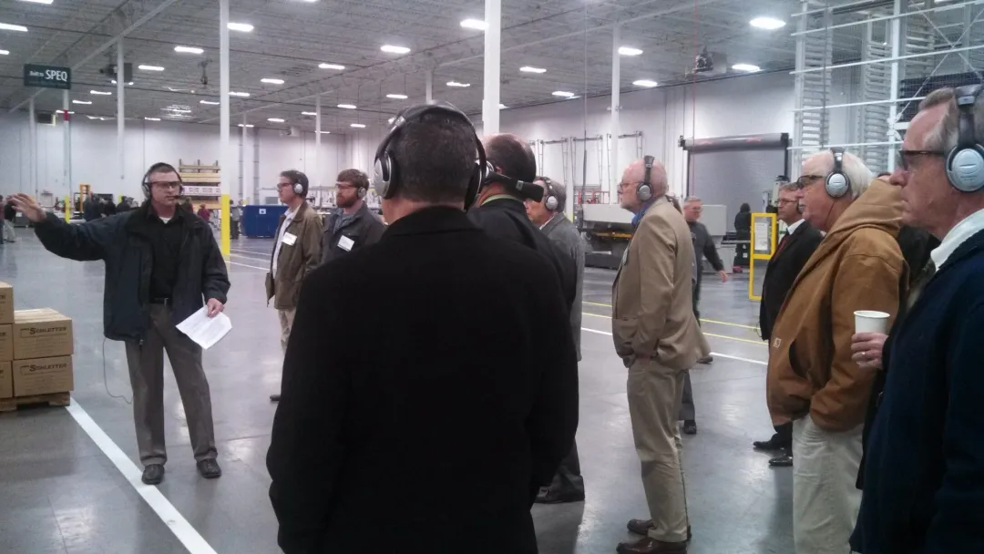 A guide leads a group wearing headsets through a warehouse