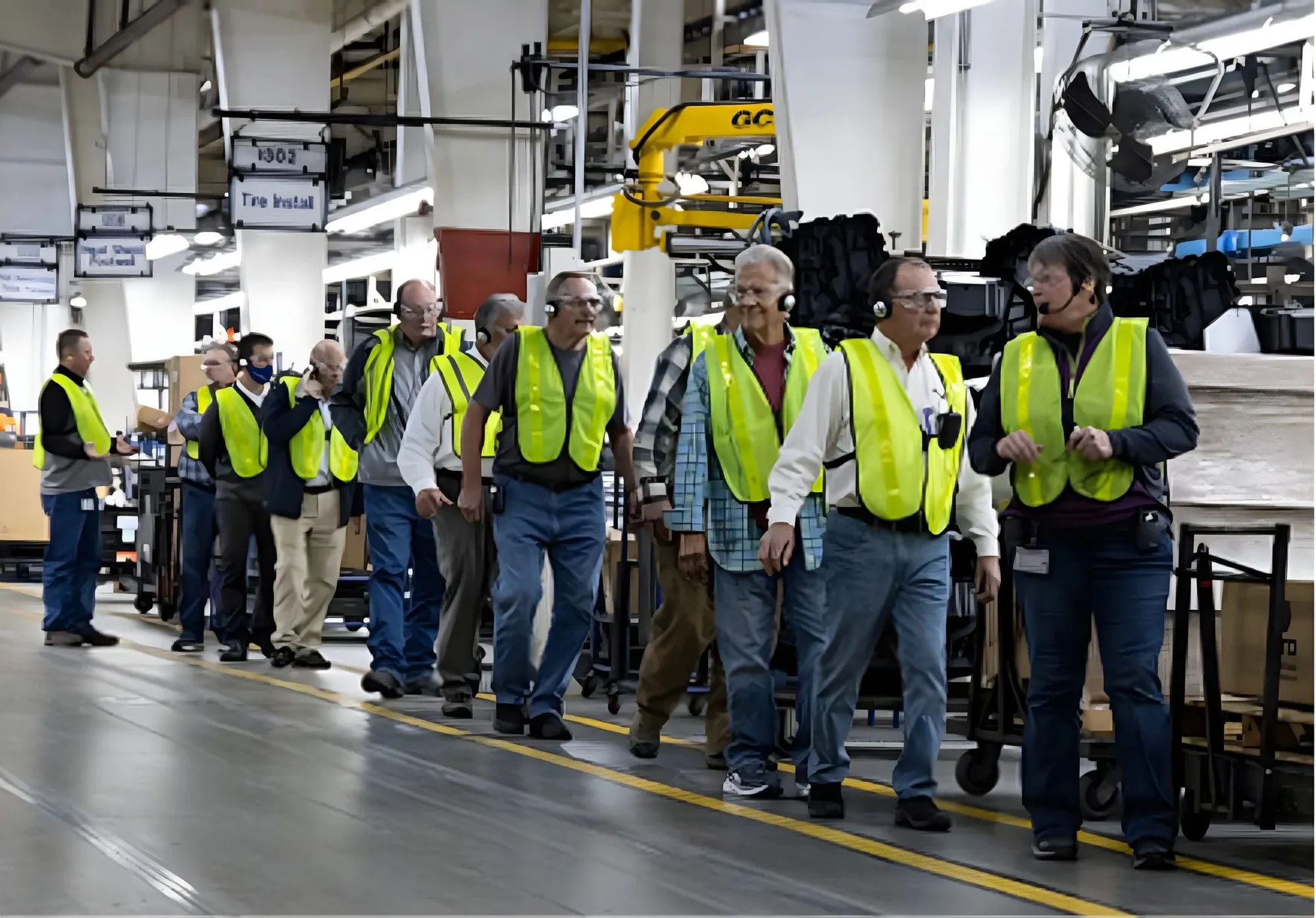 Visitors in safety vests wearing headsets on a walkthrough of a production floor