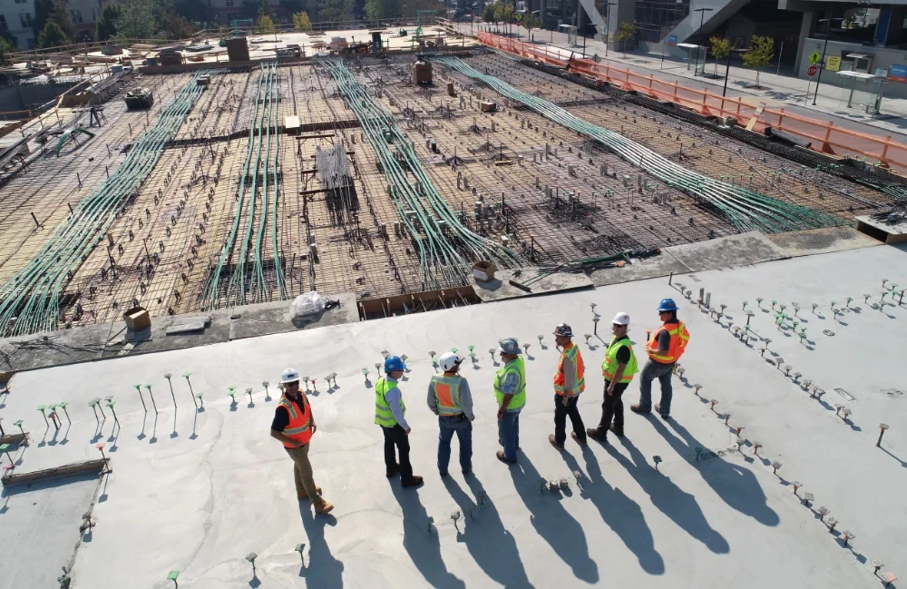 Aerial view of workers in hard hats and hi-vis vests standing on a large construction site