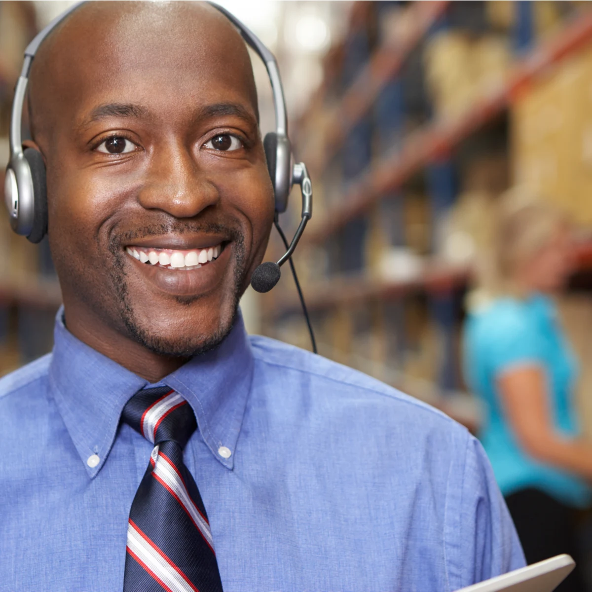Smiling man in a shirt and tie wearing a headset in a warehouse