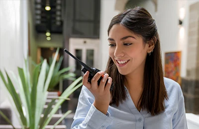 Smiling woman talking into a two-way radio in a hotel lobby