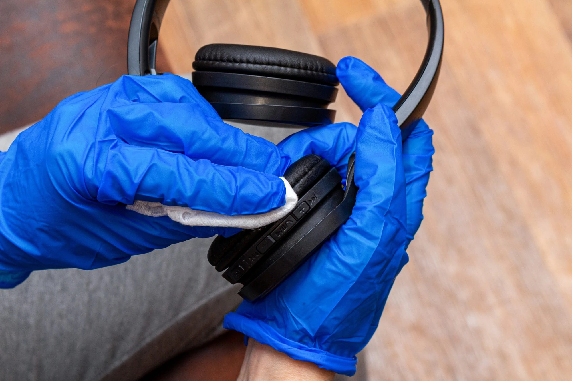 Hands in blue disposable gloves wiping the ear cushion of a black headset with a cloth