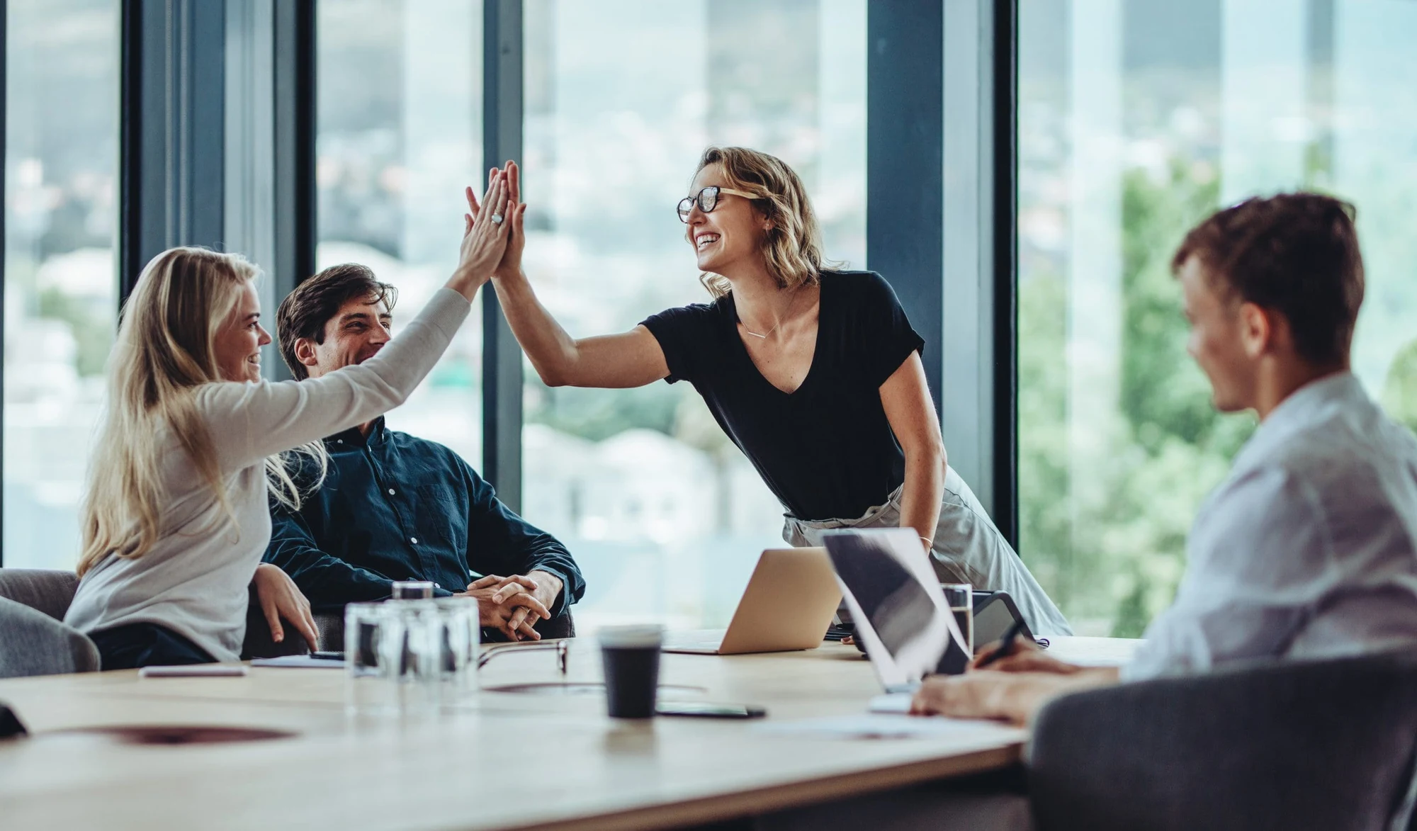 Colleagues around a meeting table, two women exchanging a high five