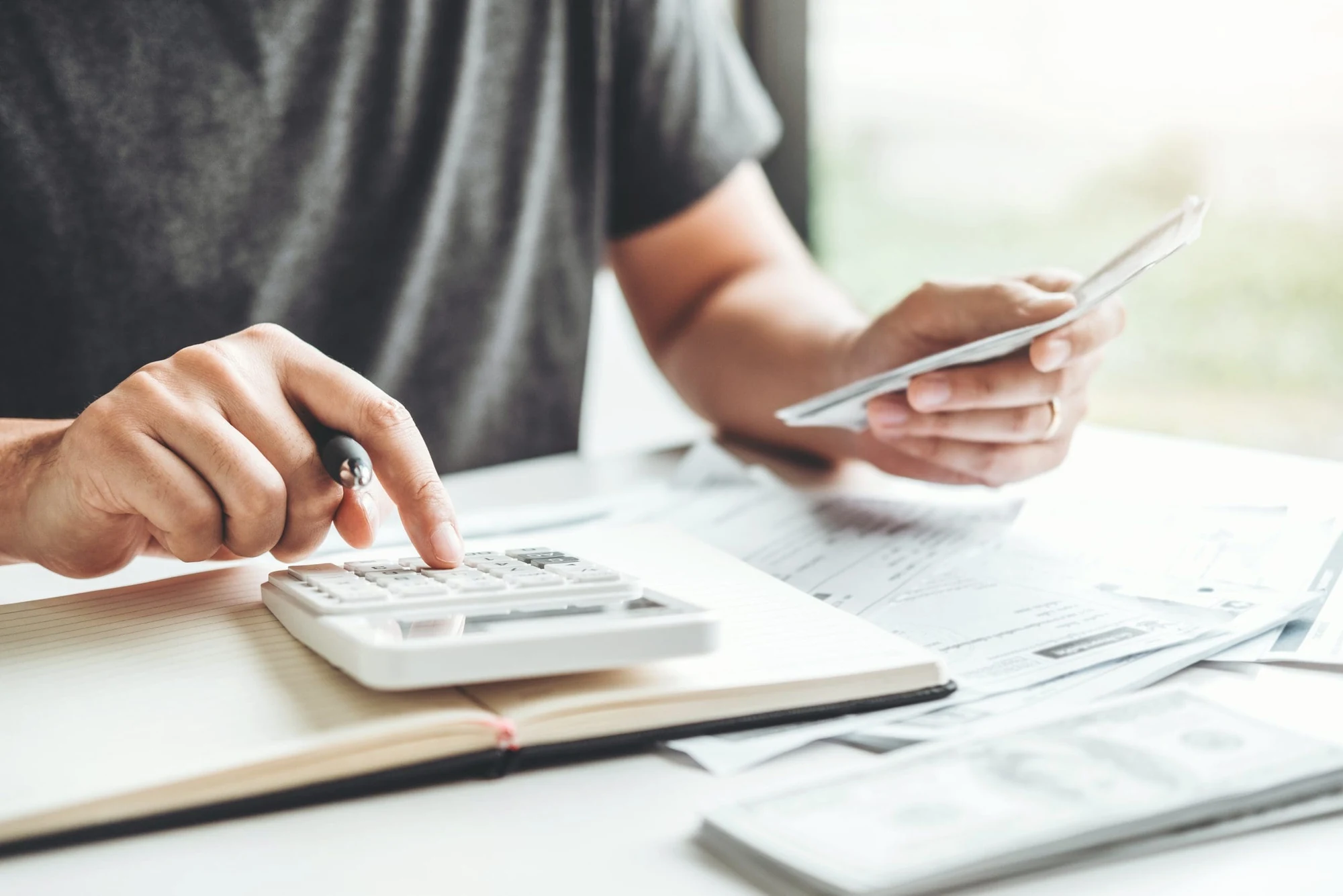 Person using a calculator while reviewing paperwork and a phone at a desk