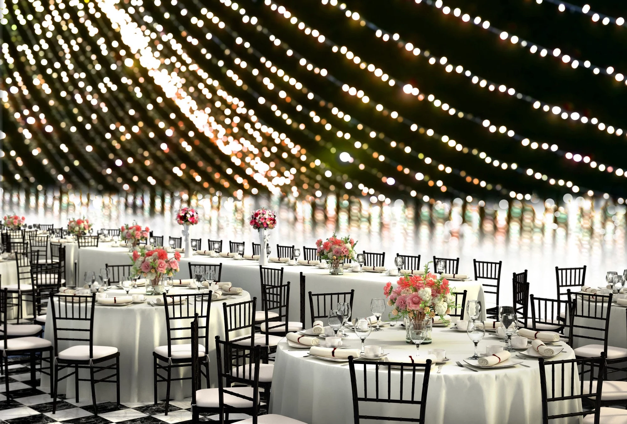 Event hall with round tables, flower centerpieces and strings of lights across the ceiling