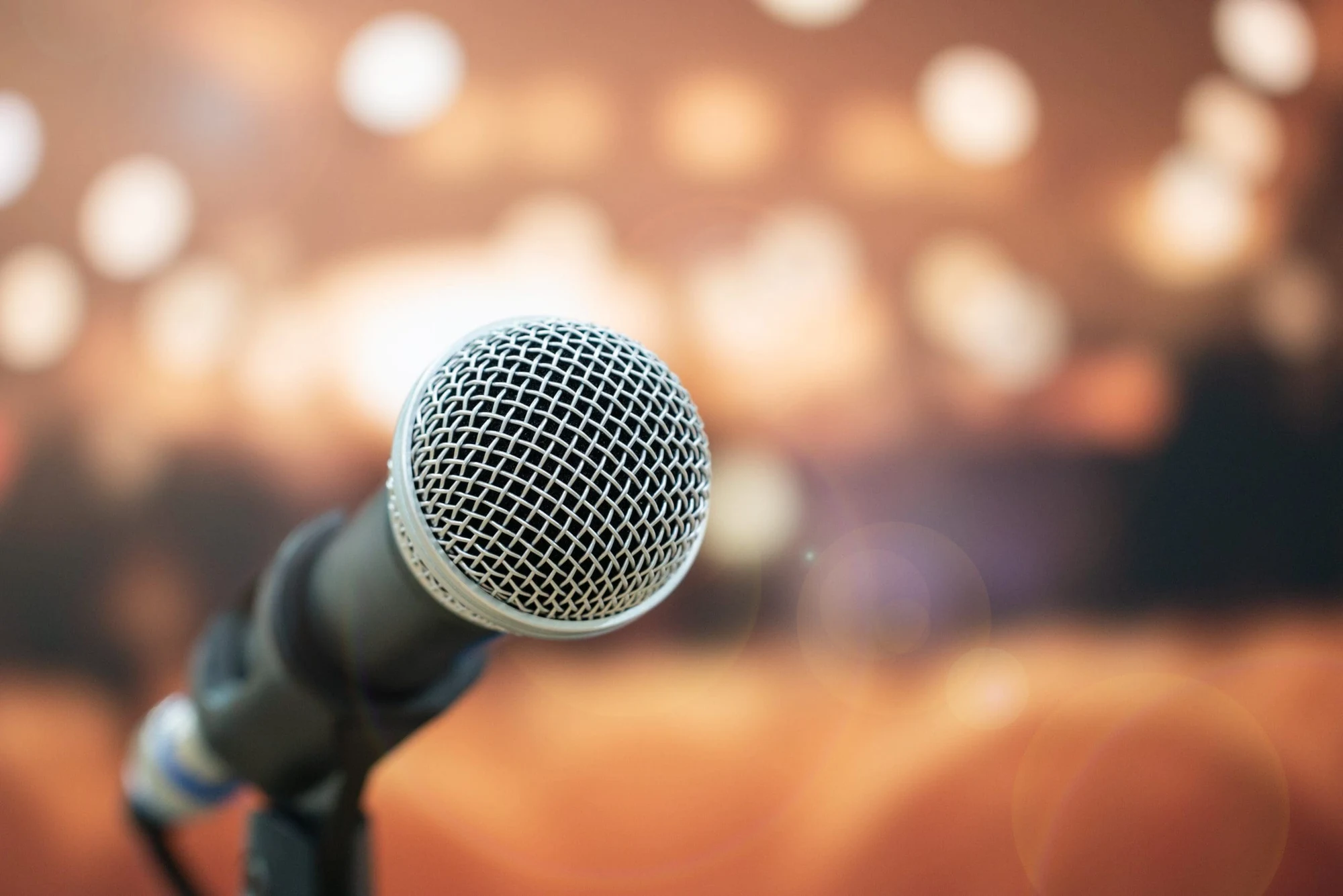 Microphone on a stand in front of a blurred stage with warm bokeh lights