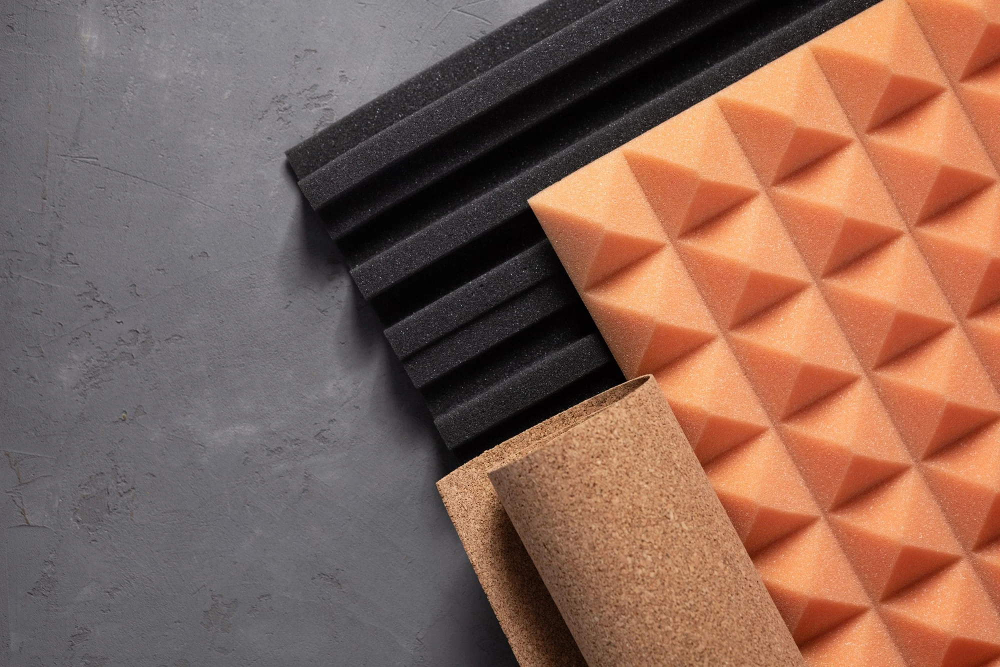 Samples of acoustic foam panels and cork sheet on a gray surface