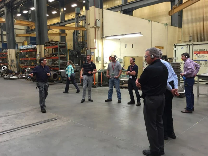 Group of visitors standing on the floor of a large factory during a plant tour
