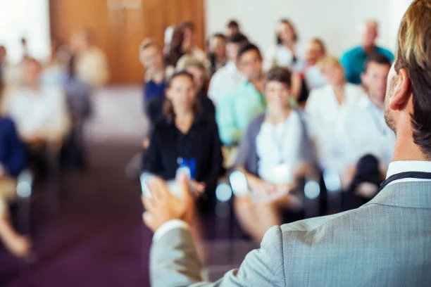 Speaker addressing a seated audience at a conference, seen from behind