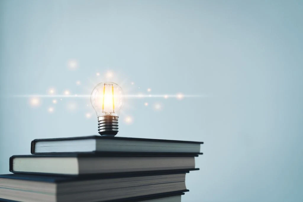 Glowing lightbulb resting on a stack of books