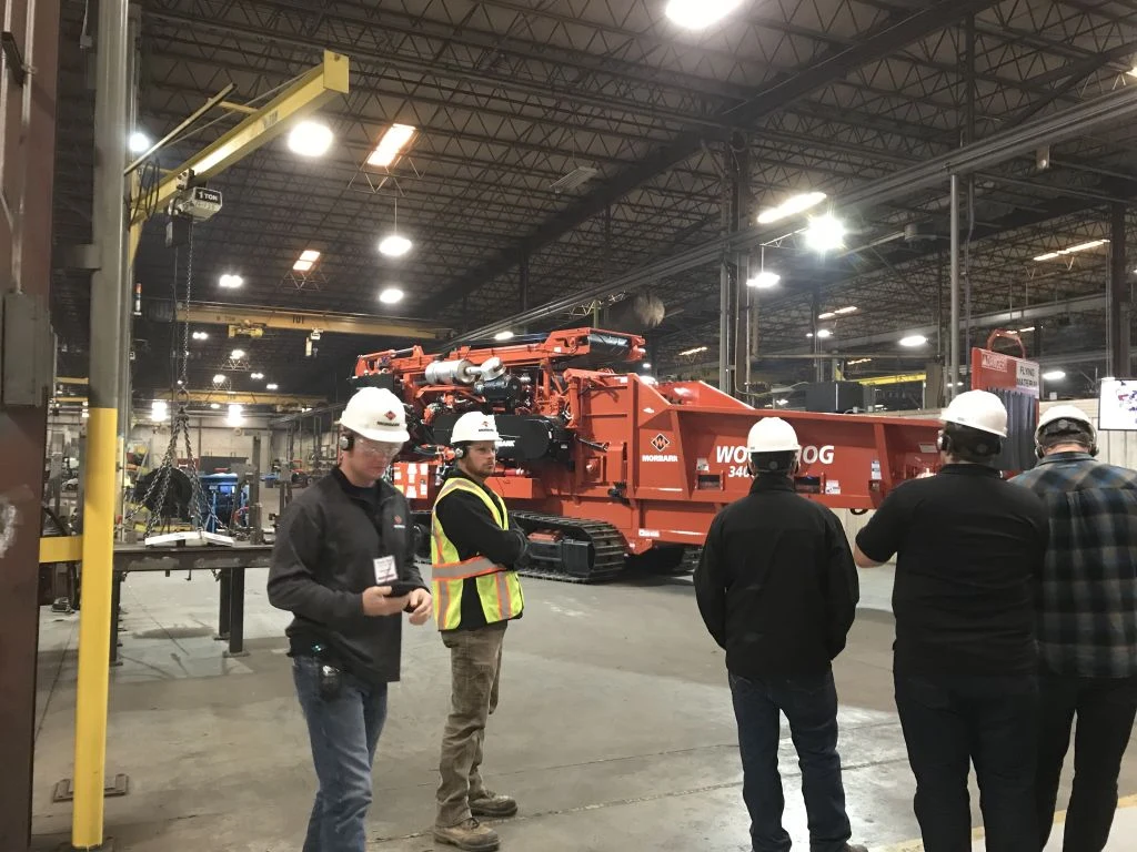Visitors in hard hats and safety vests standing near large red machinery in a factory