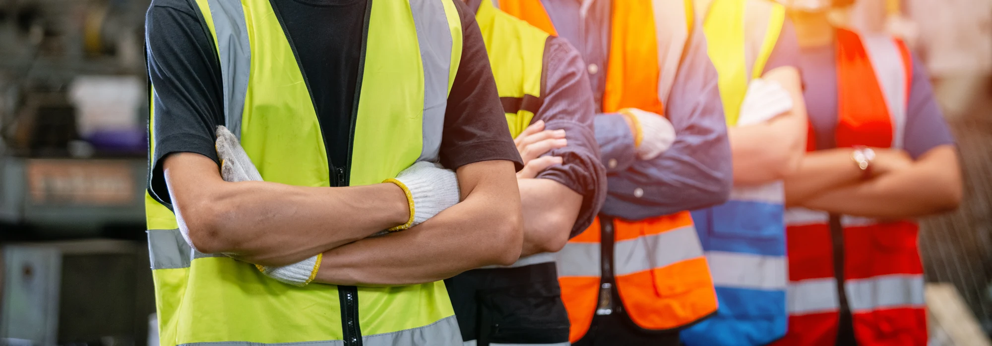 Row of workers in high-visibility safety vests standing with arms crossed