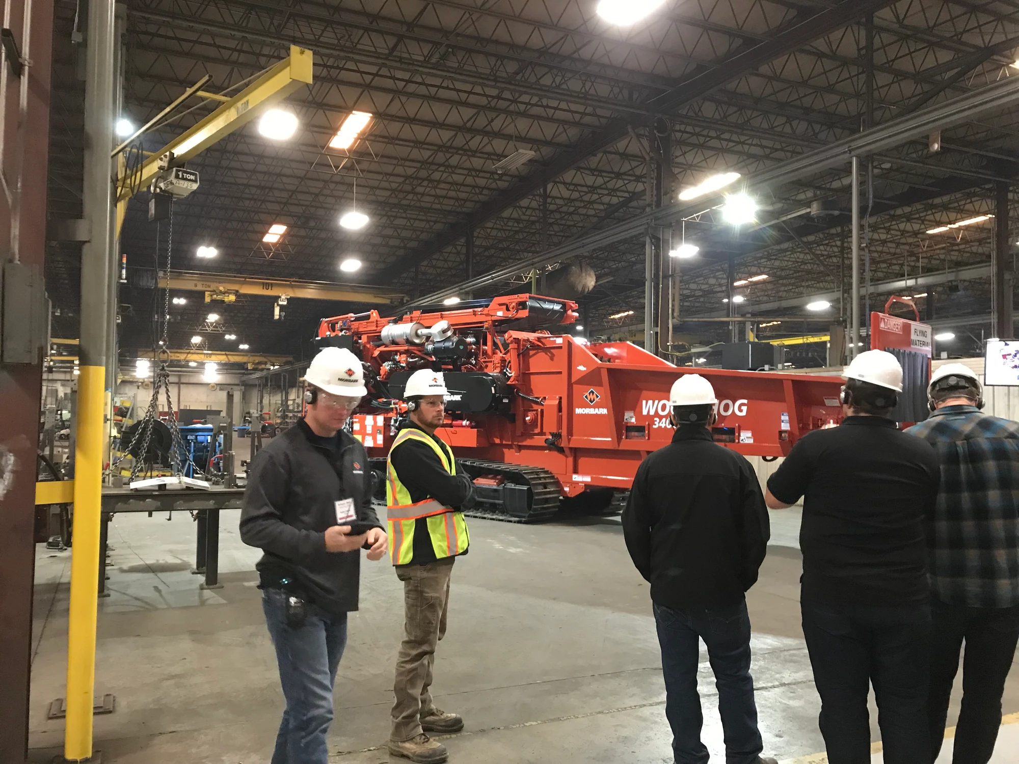 Group in hard hats and safety vests on a tour of a factory floor near large machinery