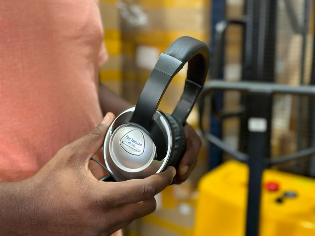 Hand holding a pair of silver and black over-ear headphones in an industrial setting