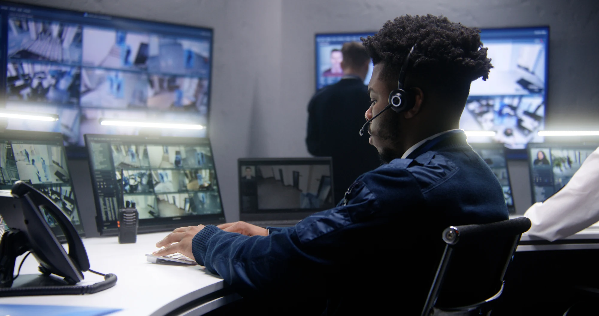 Security operator wearing an earpiece monitoring a wall of CCTV screens