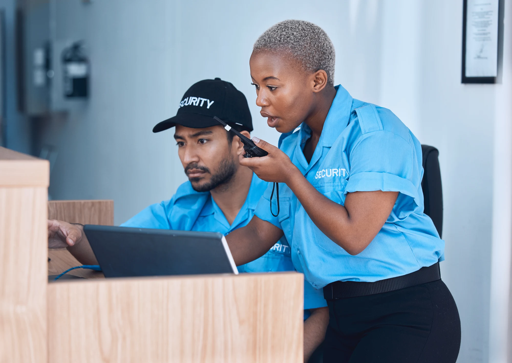 Two security staff in blue uniforms at a desk, one talking on a two-way radio