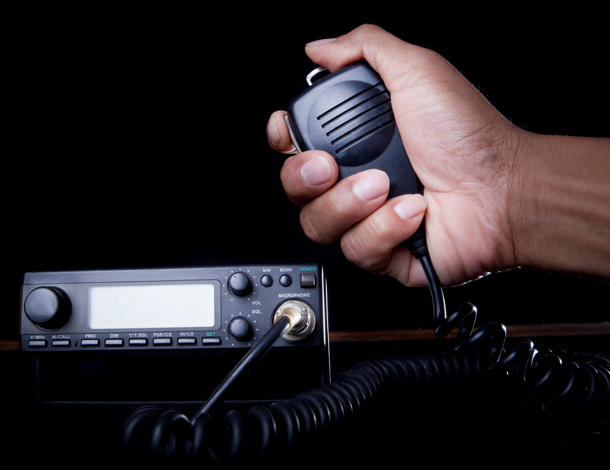 Hand holding a handheld microphone connected to a mobile radio unit