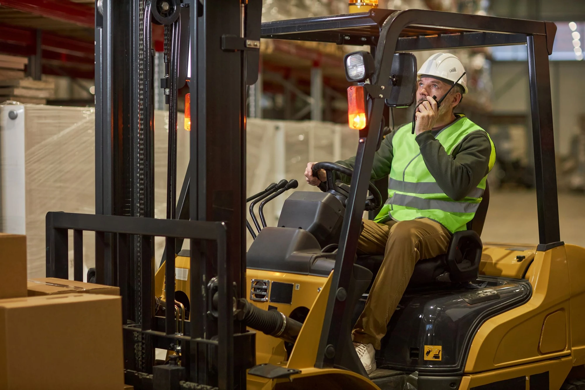 Forklift driver in hard hat and hi-vis vest talking on a radio in a warehouse